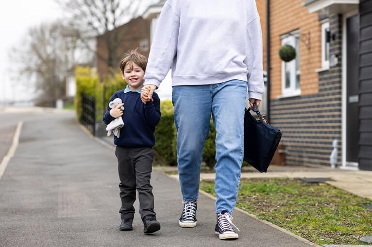 A young boy in a school uniform walking down the street and holding hands with a parent