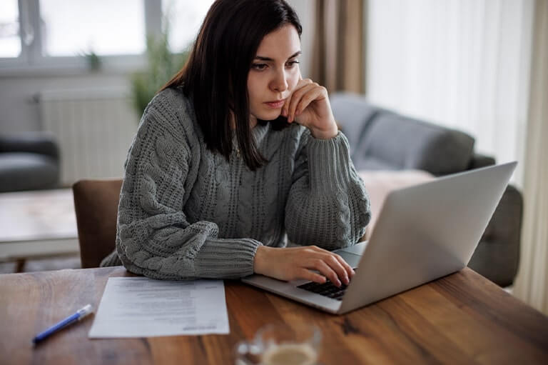 A woman with brown hair looking at a laptop and filling out paperwork