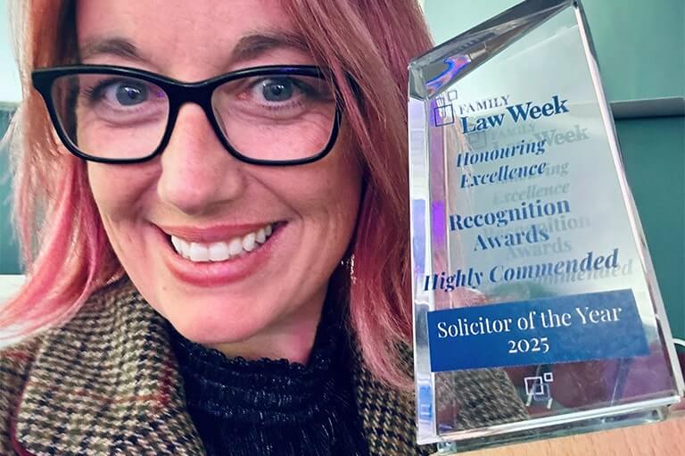 Woman with pink hair and glasses holding up an award that says solicitor of the year 2025